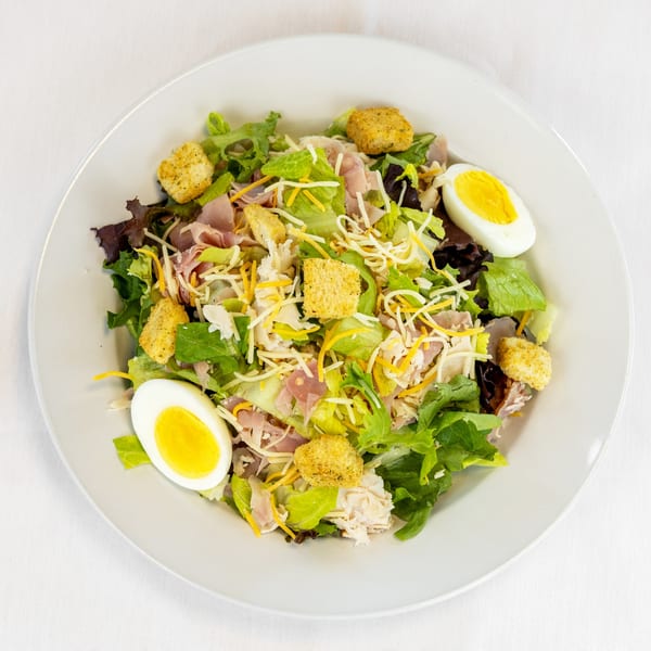Overhead view of a chef salad with lettuce, ham, cheese, croutons, and hard-boiled eggs.