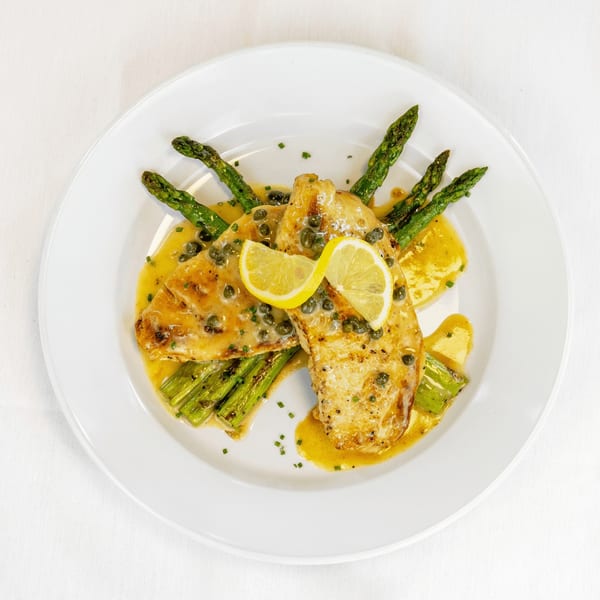 Chicken piccata with capers, lemon slices, and asparagus, drizzled with sauce on a white plate.