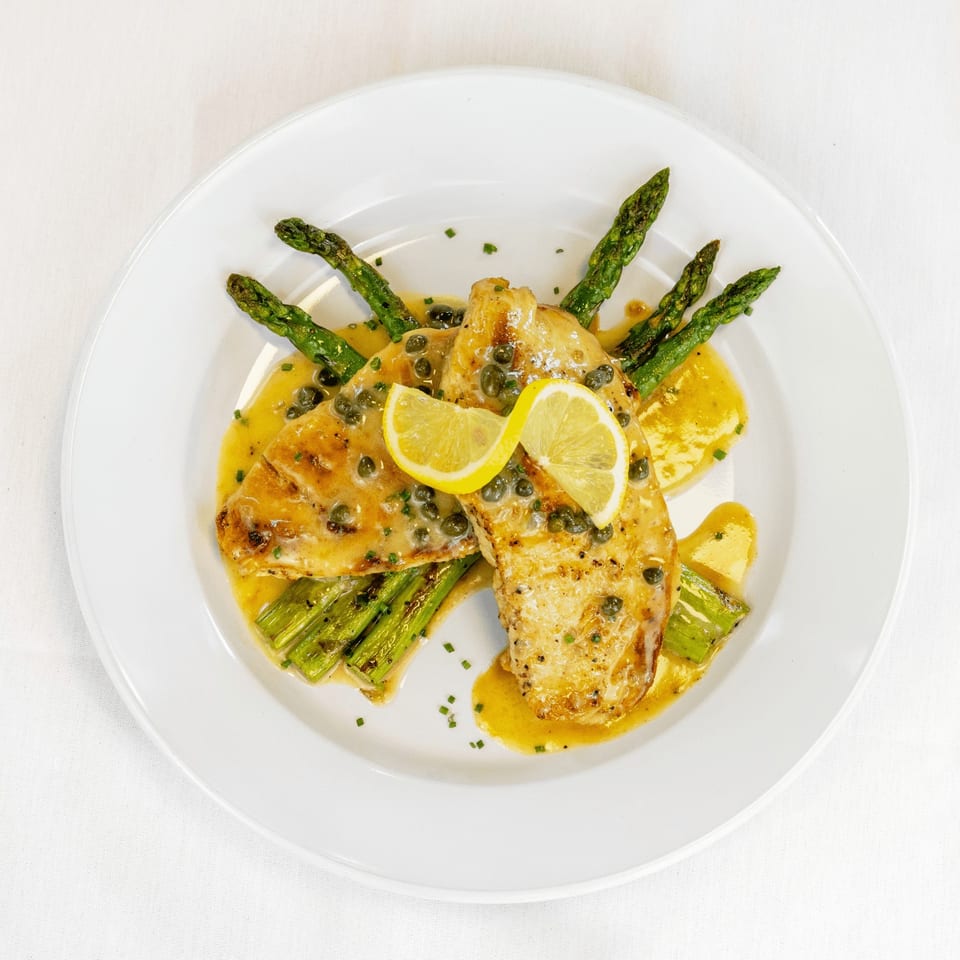 Chicken piccata with capers, lemon slices, and asparagus, drizzled with sauce on a white plate.