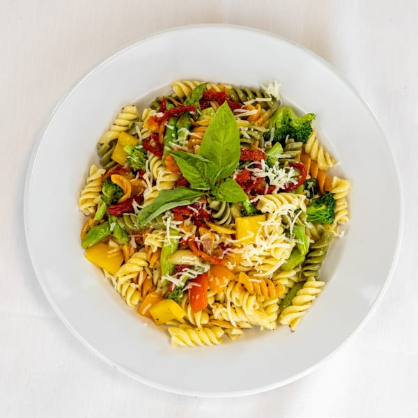 Colorful fusilli pasta salad with vegetables, cheese, and basil on a white plate.