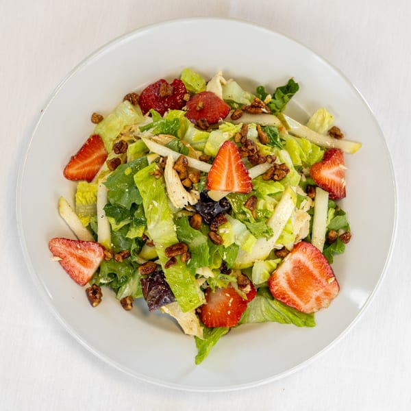 Overhead view of a fresh salad with lettuce, strawberries, nuts, and sliced pears on a white plate.