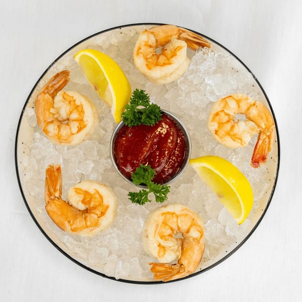 Shrimp cocktail with six large shrimp, cocktail sauce, lemon wedges, and parsley on a bed of ice.