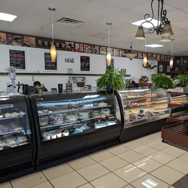 Interior of a bakery with display cases full of cakes and pastries, and a counter with a person behind it.
