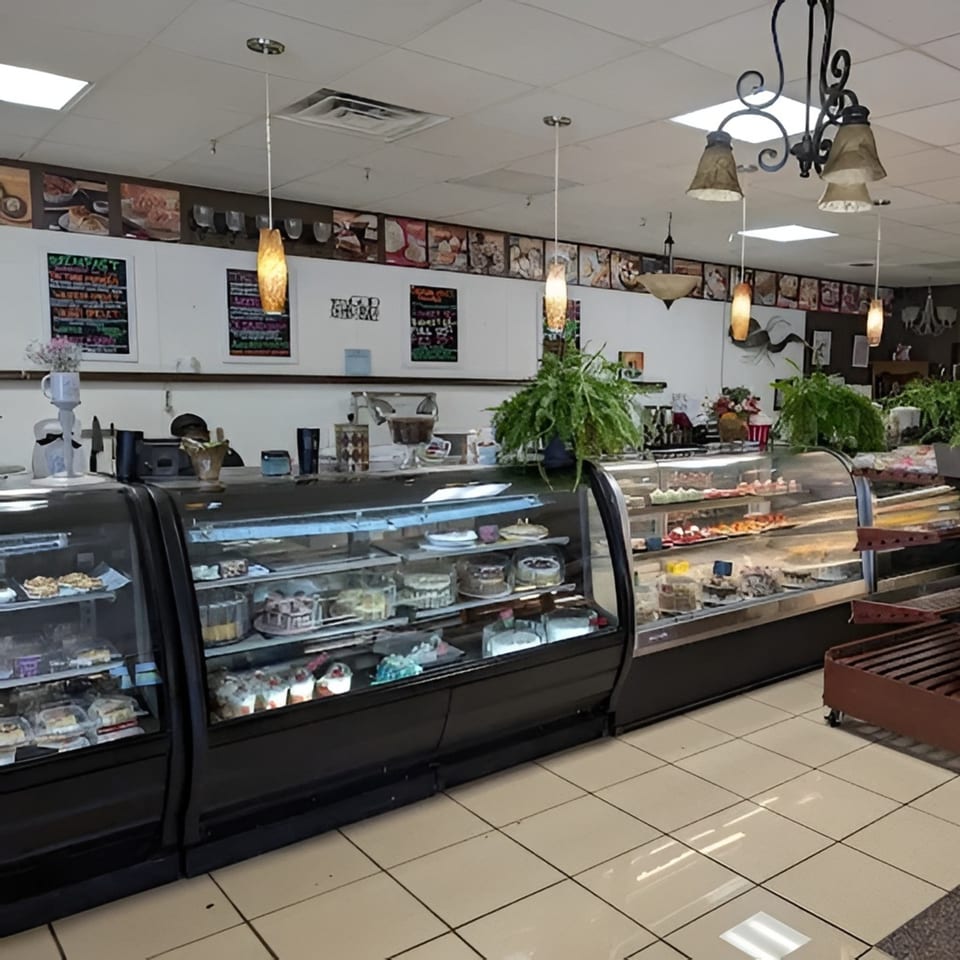 Interior of a bakery with display cases full of cakes and pastries, and a counter with a person behind it.