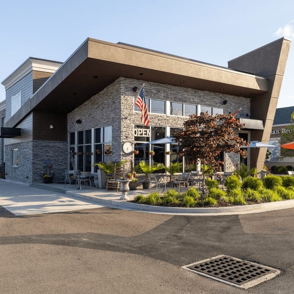 Modern restaurant exterior with stone and wood siding, outdoor seating, and an American flag.