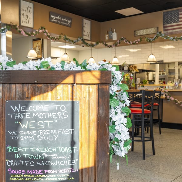 Chalkboard sign for "Three Mothers West" restaurant, with breakfast and lunch items listed.