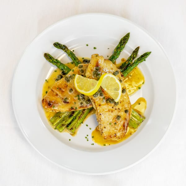 Chicken piccata with lemon slices, capers, and asparagus, drizzled with sauce on a white plate.