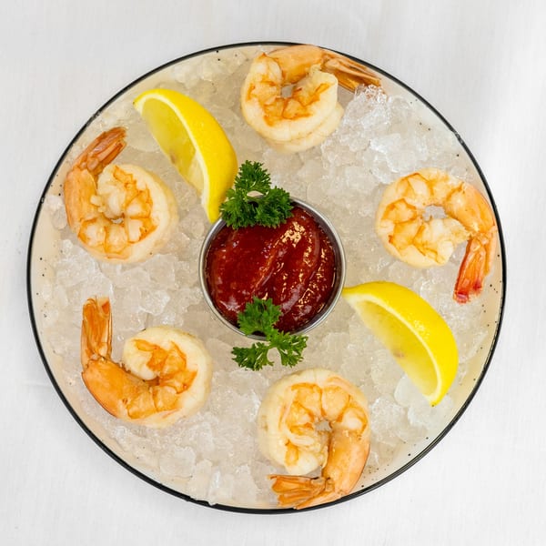 Shrimp cocktail with six large shrimp, cocktail sauce, lemon wedges, and parsley on ice.