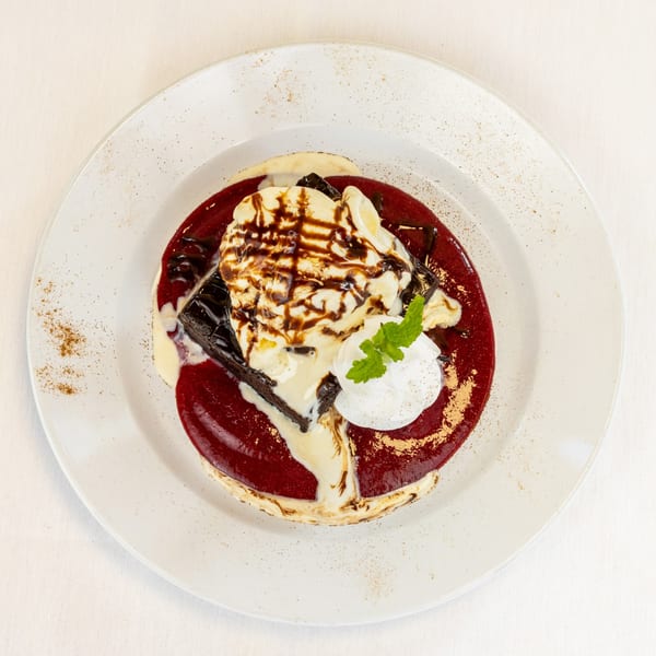 Chocolate brownie with vanilla ice cream, raspberry sauce, whipped cream, and mint on a white plate.