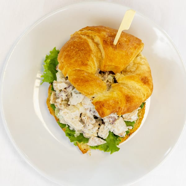 Chicken salad croissant sandwich with lettuce on a white plate, viewed from above.