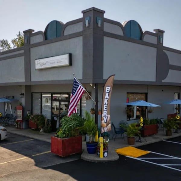 Exterior of a gray bakery building with outdoor seating, an American flag, and a "BAKERY" banner.
