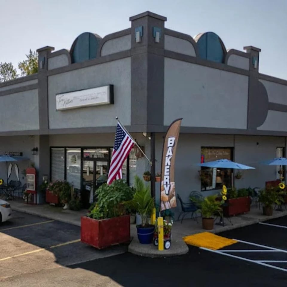 Exterior of a gray bakery building with outdoor seating, an American flag, and a "BAKERY" banner.